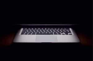 Halb aufgeklapptes, leuchtendes Apple MacBook auf schwarzem Hintergrund